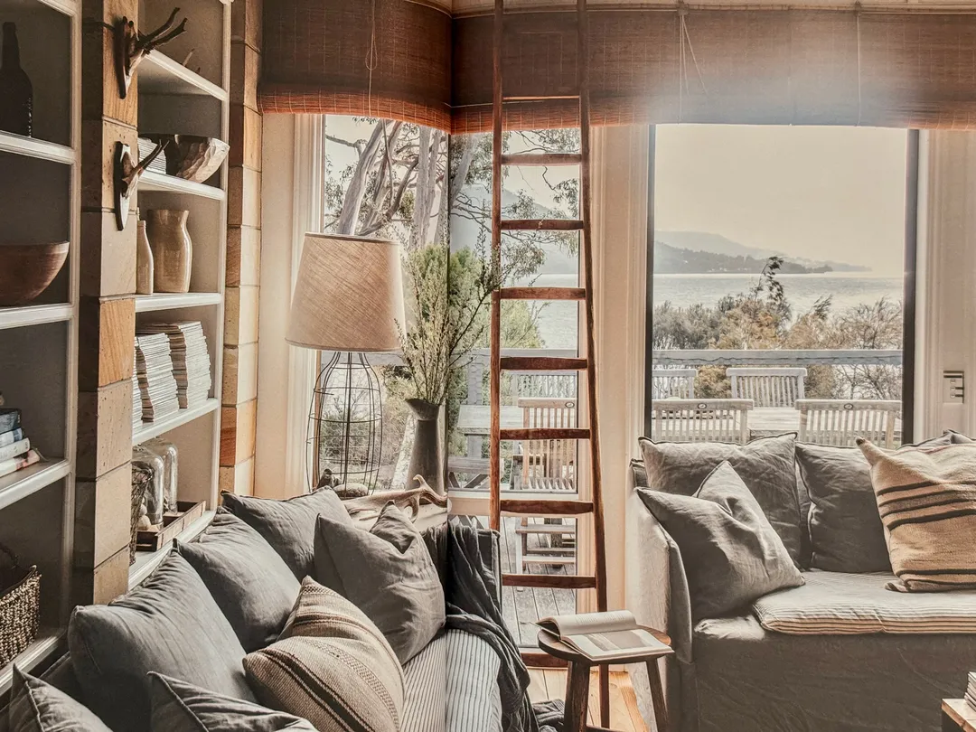 Living room with grey sofas, tall bookshelves and a library ladder by the sea