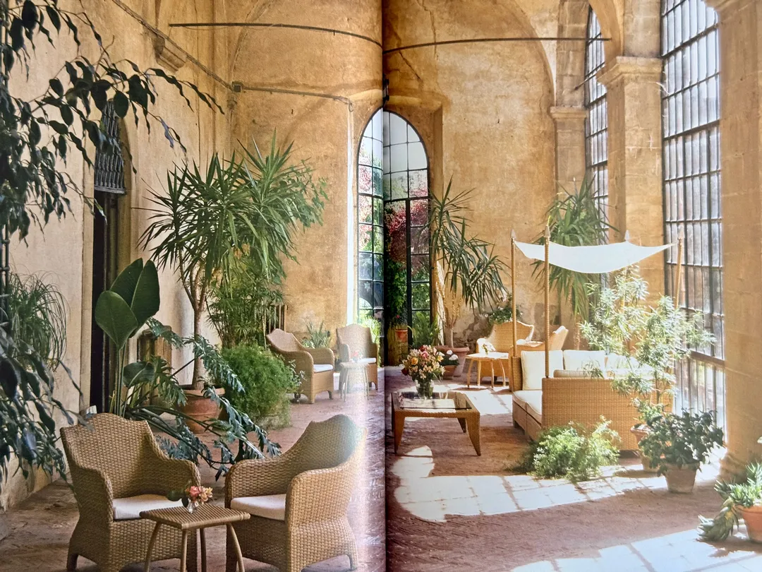 Arched glasshouse lounge filled with potted plants and rattan chairs