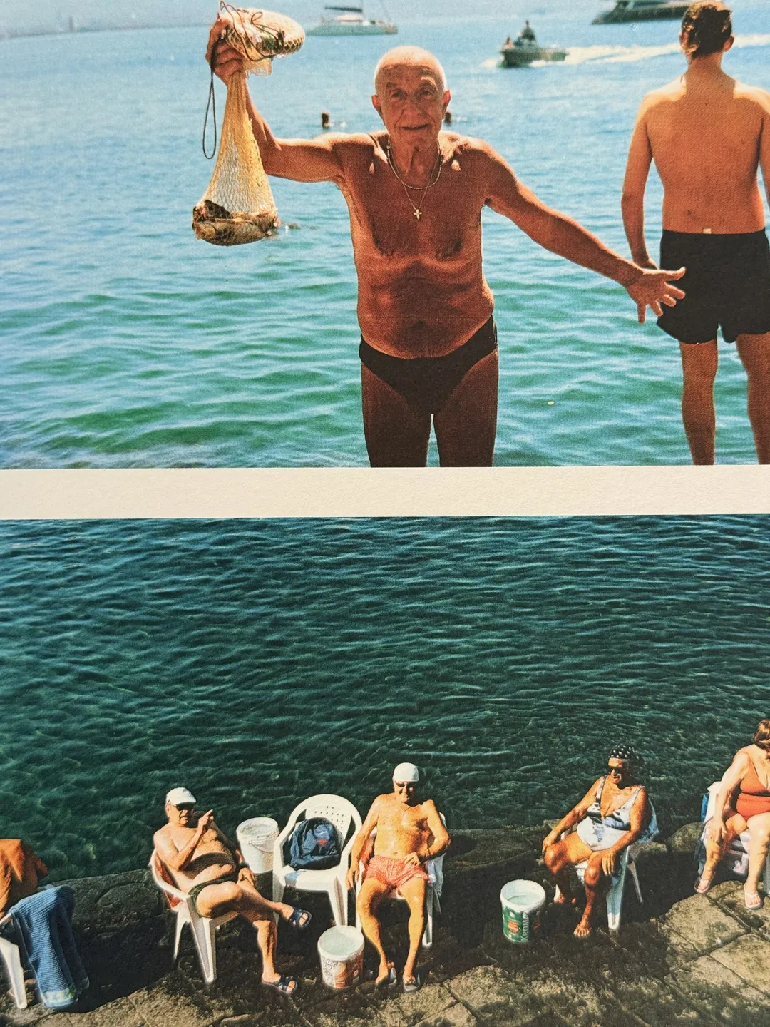 Older man in swim trunks holding up his catch, and bathers on plastic chairs by the water