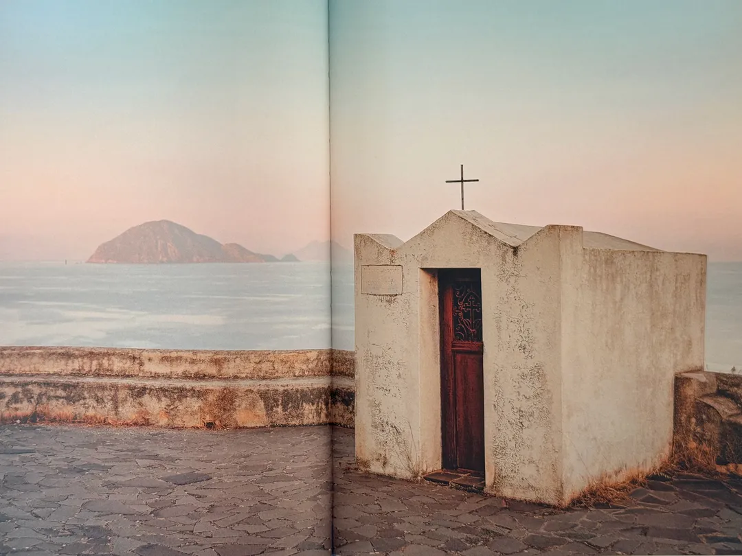 Small whitewashed chapel by the sea with an island on the horizon