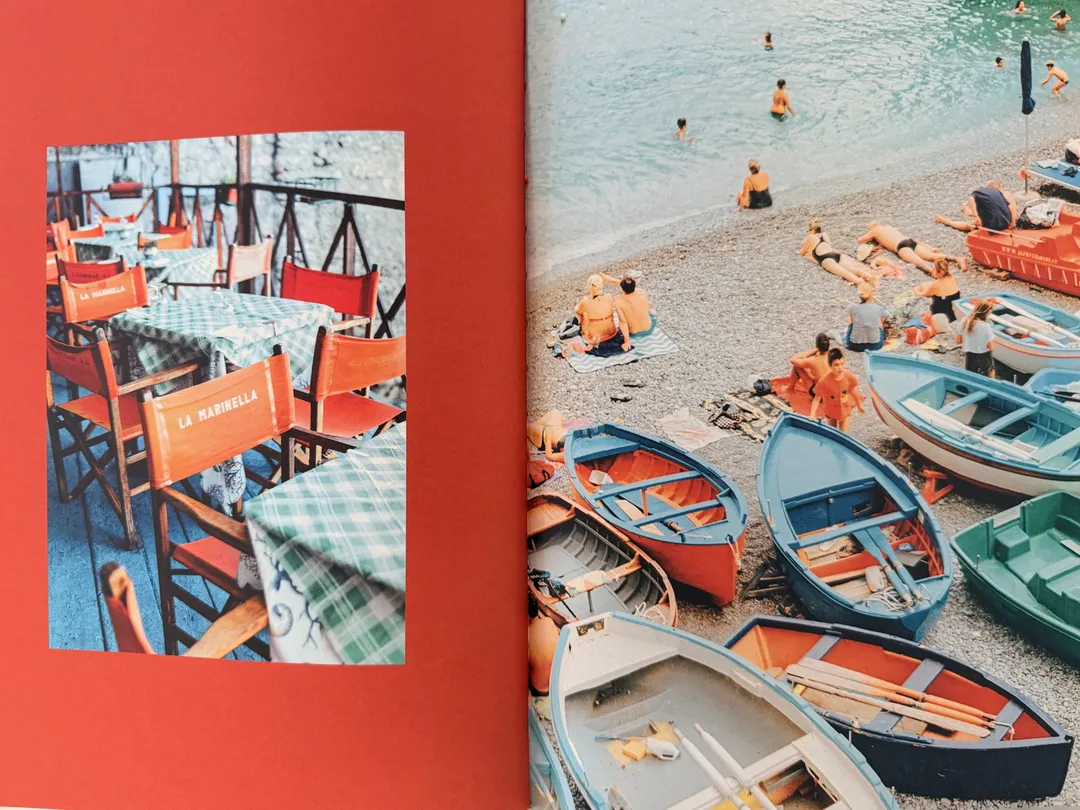 Rowboats on a pebble beach beside red café chairs
