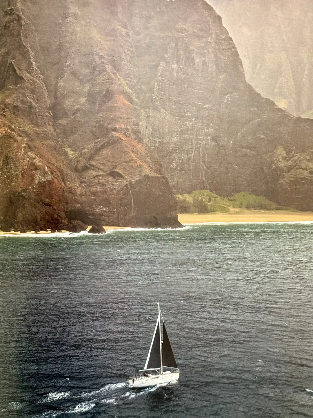 Lone sailboat beneath towering green sea cliffs