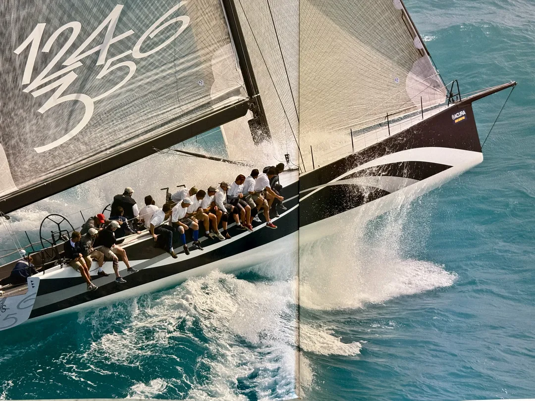 Crew lined along the rail of a racing yacht heeling through spray