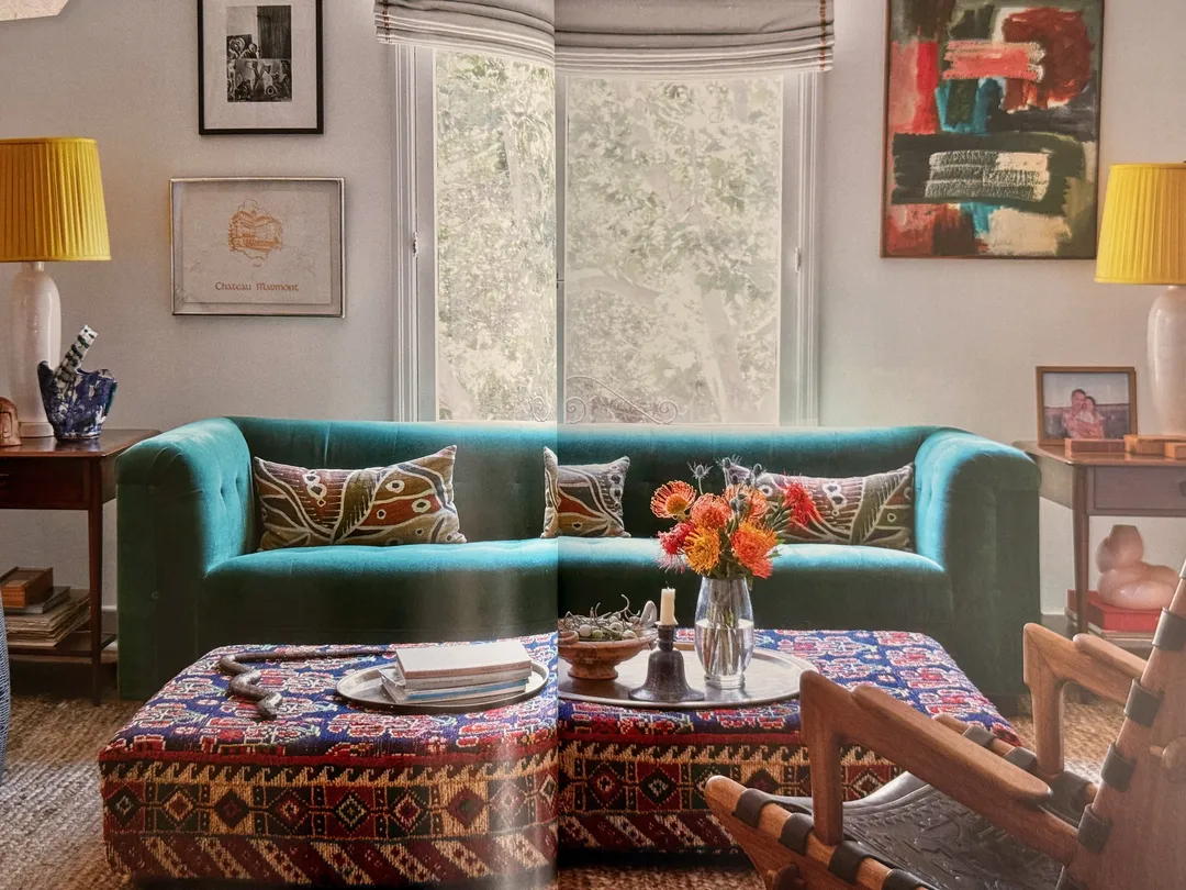 Living room with a teal velvet sofa, kilim ottoman and yellow lamps