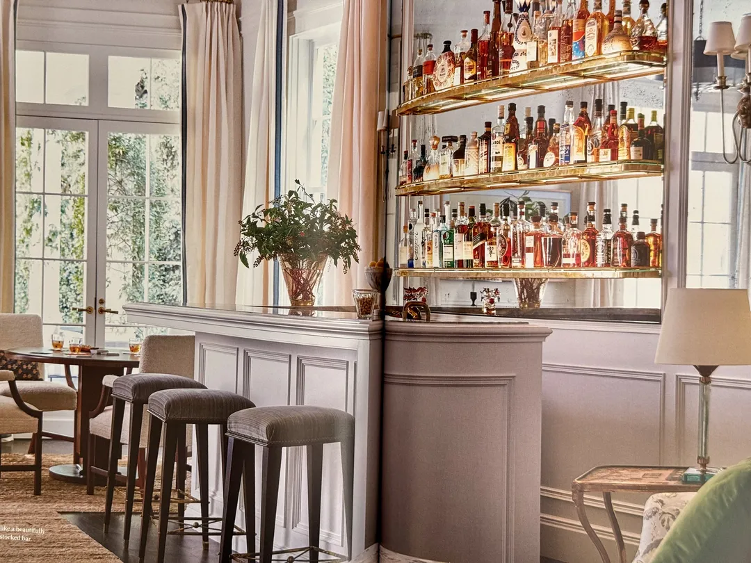 Home bar with brass shelves of bottles and upholstered stools