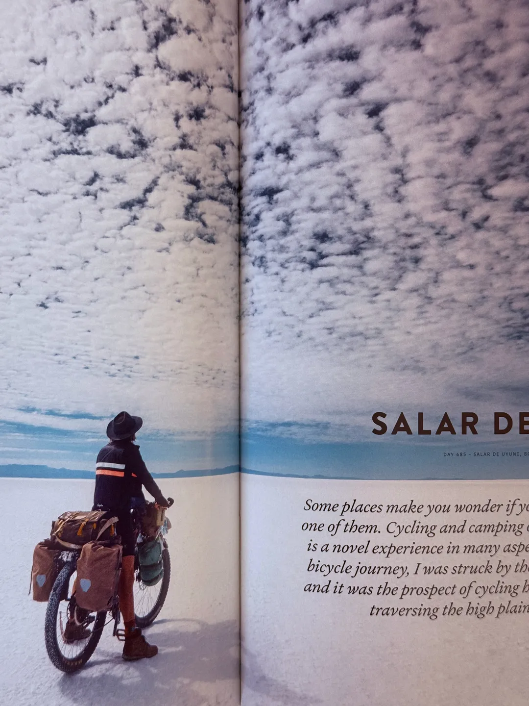 Cyclist with a loaded touring bike on a salt flat under a cloud-streaked sky, from Two Years on a Bike